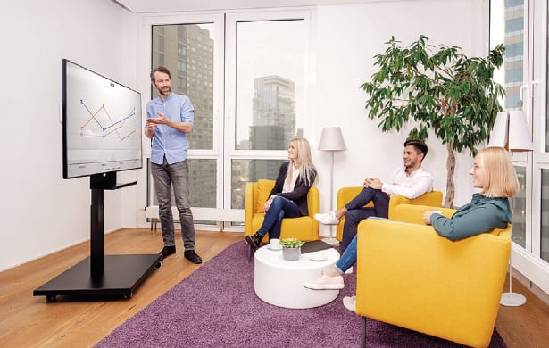 man delivering presentation on freestanding monitor to three people